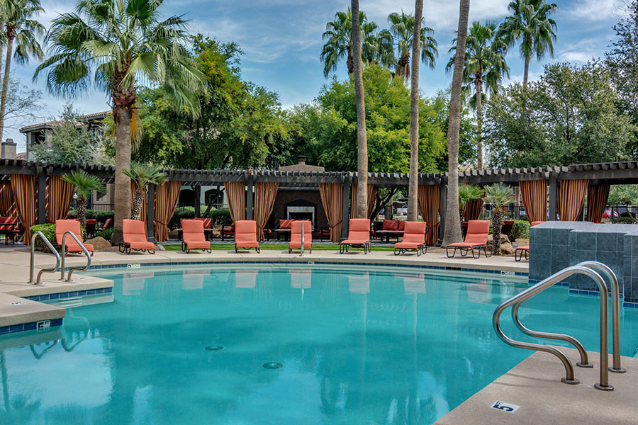 Arizona Community Mesa pool with lounge chairs, palm trees, and long pergola with fireplace encircling deep blue pool.