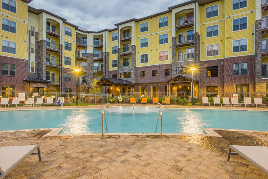 North Carolina five story apartment overlooking brightly lit pool area with smooth stone and lounge chairs.