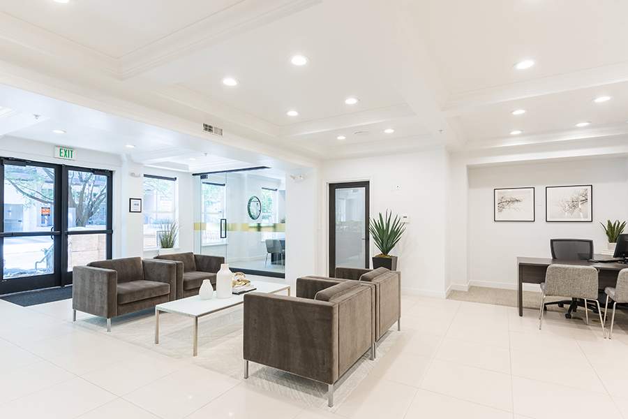 Brightly lit office with modern lounge chairs and coffee table, desk with chairs and computer, and glass entry doors.