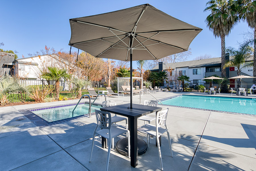 view of outdoor table shaded by big umbrella and in background the pool and Jacuzzi with modern pergolas and loungers