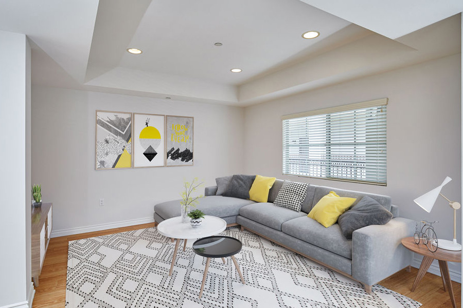 living room space hardwood floors a white patterned rug with grey sectional couch and yellow pillows