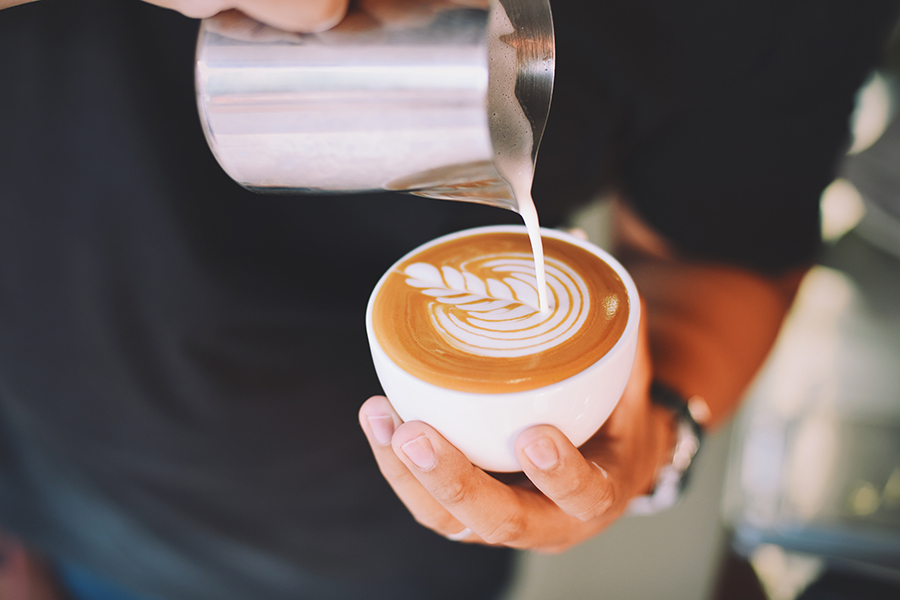 Person pouring decorative floral pattern with milk into coffee.