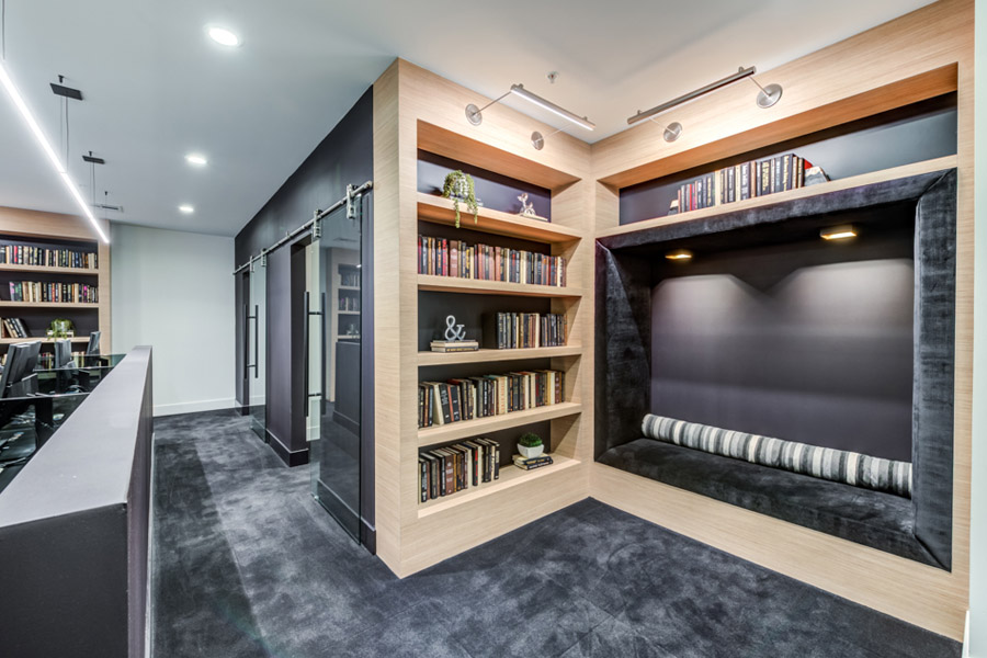 lounge area with a bookshelf on fine light wood and in the other wall a plush reading nook with black fabric seats and a marbled black grey carpet