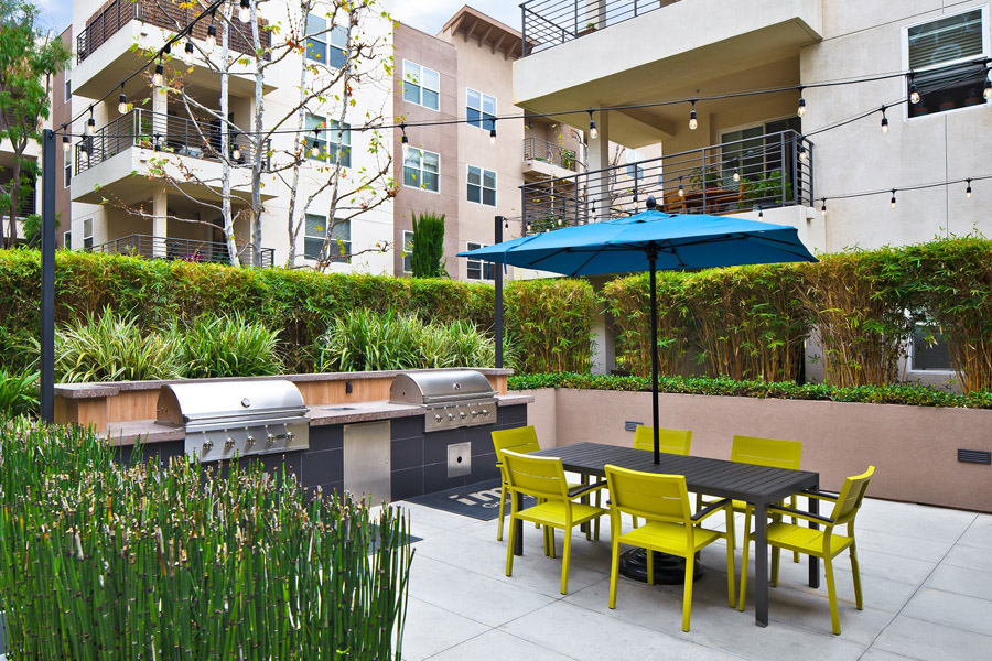 outdoor grilling area with two stainless steel grills and a patio table with neon green chairs and bright blue umbrella