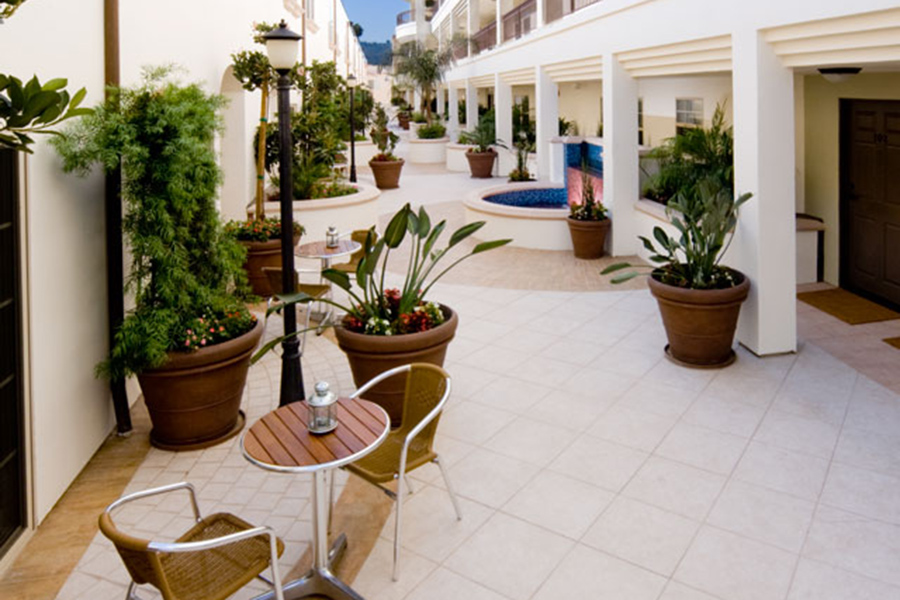 Outdoor courtyard with tile floors, large potted plants, small tables, and tiled fountains.