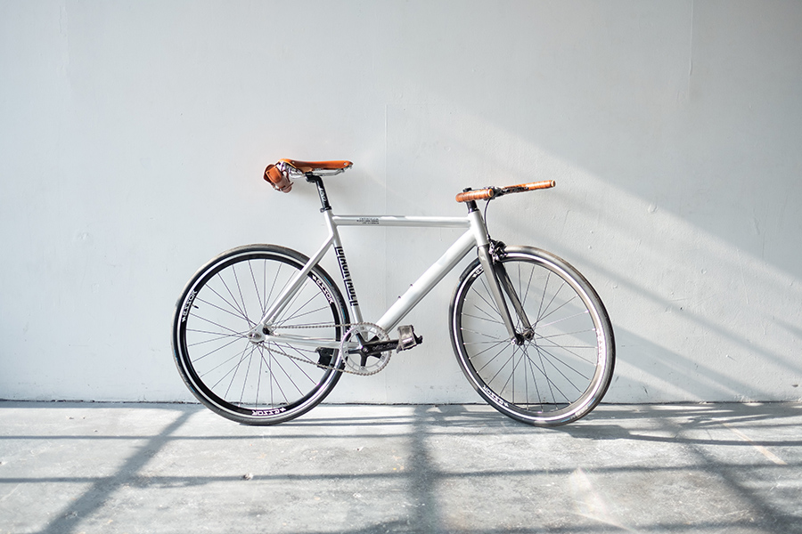 Single speed bicycle leaning against white wall in bright sunlight.