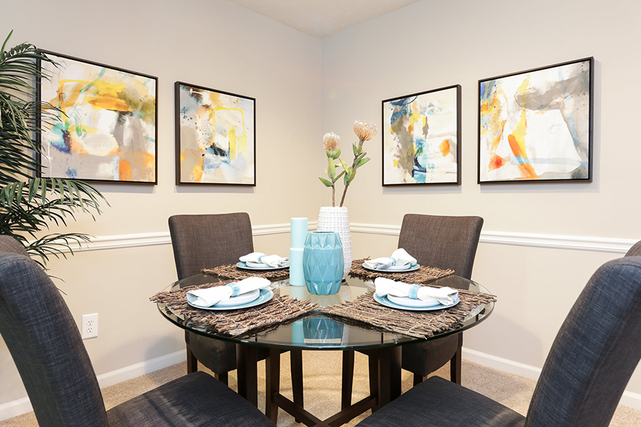 Apartment dining area with wall art, round dining table with place settings, and four tall chairs.