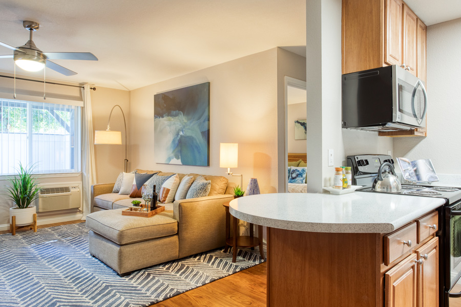 warm lighting apartment interior plush cream couch with striped rug half view of kitchen with updated appliances and rich wood cabinets