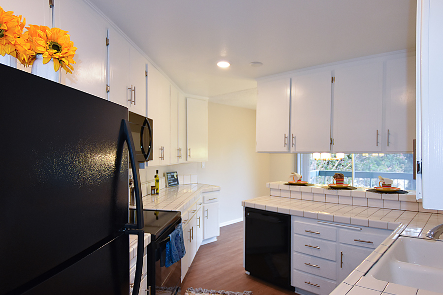 IMT Valleyheart - kitchen area in apartment with black updated appliances, tile countertops, and white cabinets