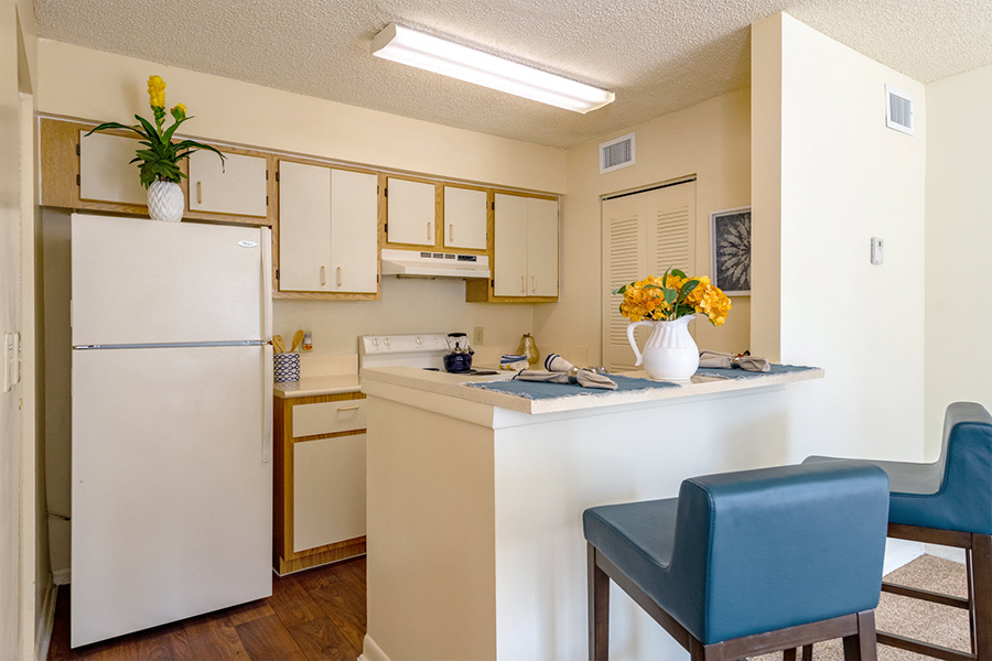 Apartment kitchen with built in breakfast bar, tall leather stools, and wood floors.