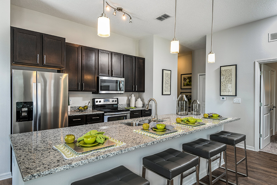 Apartment kitchen with smooth stone counters, rich wood cabinets, and stainless steel appliances.
