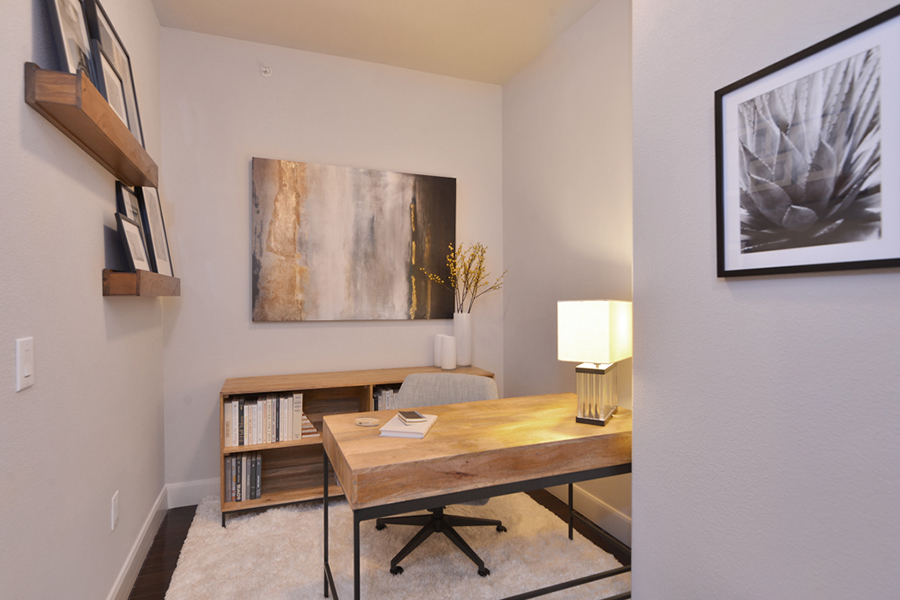 Apartment office space with bookcase, wall art, and wood desk with modern lamp.