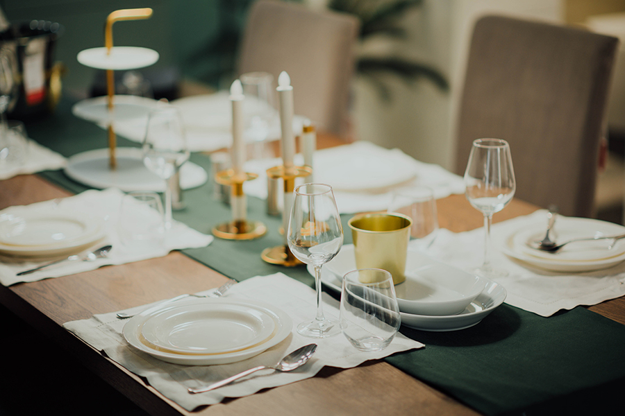 Dining table with white dining set, wine glasses, green table runner, and metal candlesticks.