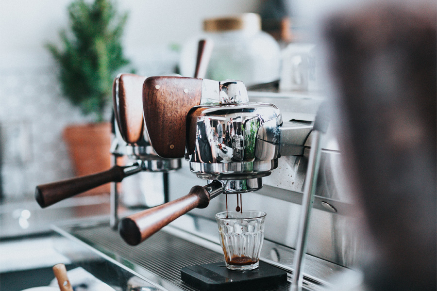 close up of stainless steel espresso machine a small glass cup catching espresso droplets