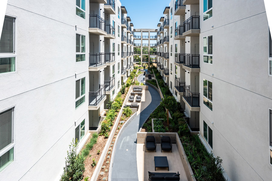 apartment patios facing each-other and in between buildings a winding pathway that leads to different outdoor lounge spaces and furniture