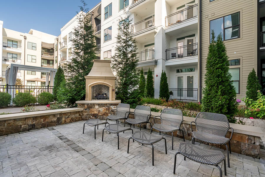 Outdoor lounge space with stone paver patio, comfortable furniture, lush landscaping, and built in fireplace.