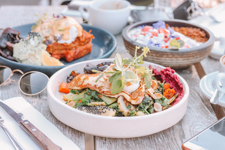 Wood picnic table with plates and bowls filled with bright, colorful food.