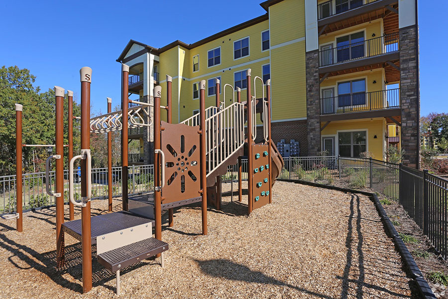 Fenced playground with metal play equipment overlooked by Ballantyne apartments.