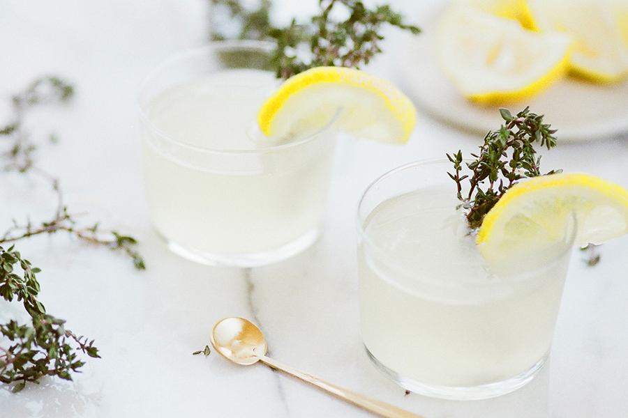 Detail of marble tabletop with cocktail glasses garnished with lemons and herbs.
