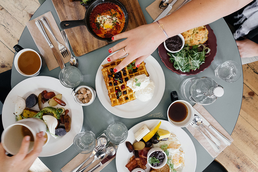 People's arms reach across round blue dining table with brunch food.