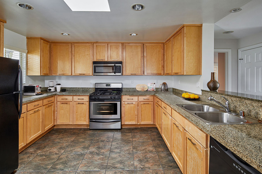Kitchen with tile floor, wood cabinets, dark counter, and glossy black appliances.