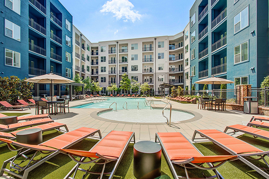 Pool area with spa and lounge chairs overlooked by apartments.