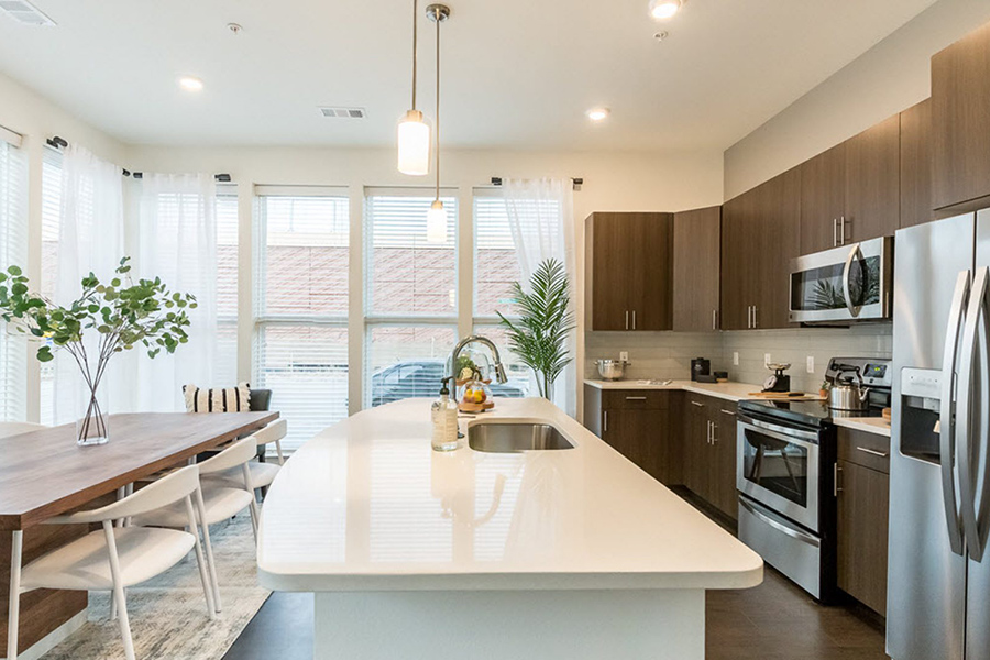 RidgeGate sustainable apartment kitchen with rich wood cabinets, bright stone countertops, and stainless steel appliances.