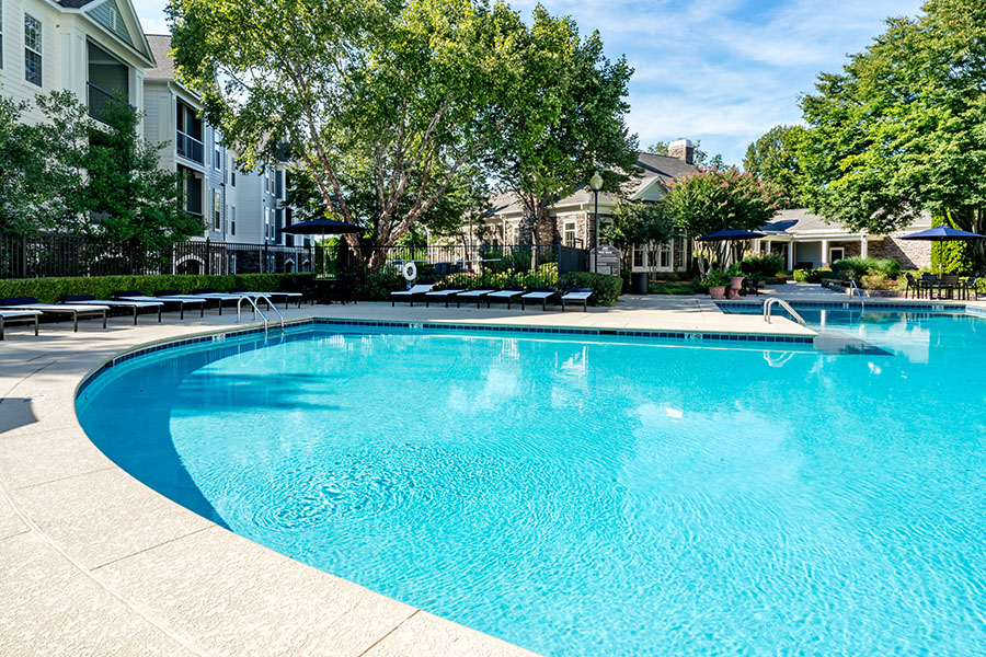 Pool area with bright blue water and stone patio surrounded by trees and overlooked by apartment balconies.
