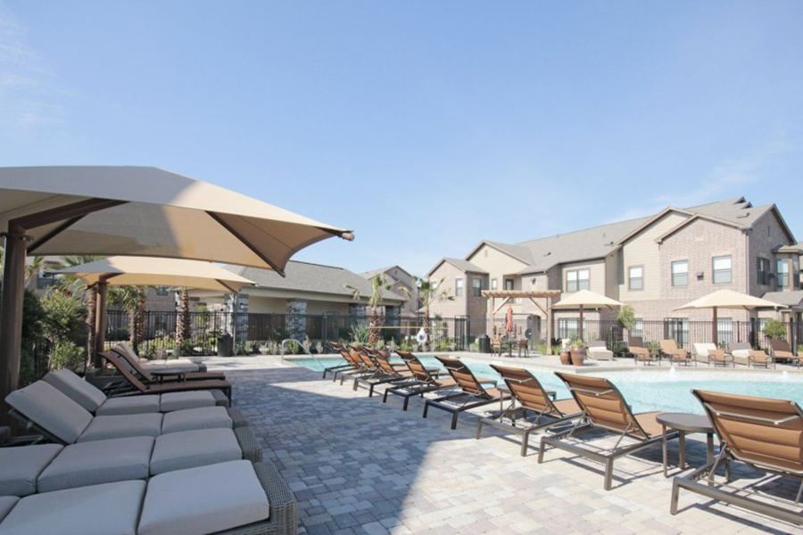 Pool area with stone patio, plush lounge chairs, and umbrellas overlooked by Cinco Ranch apartments.