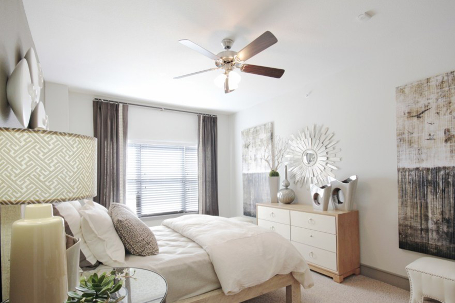 Bedroom with carpet floor, plush platform bed, wood furniture, wall artwork, and large window with curtains.