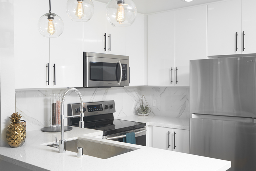 Apartment kitchen with white cabinets and counters, stainless steel appliances and sink, and retro pendant lights.