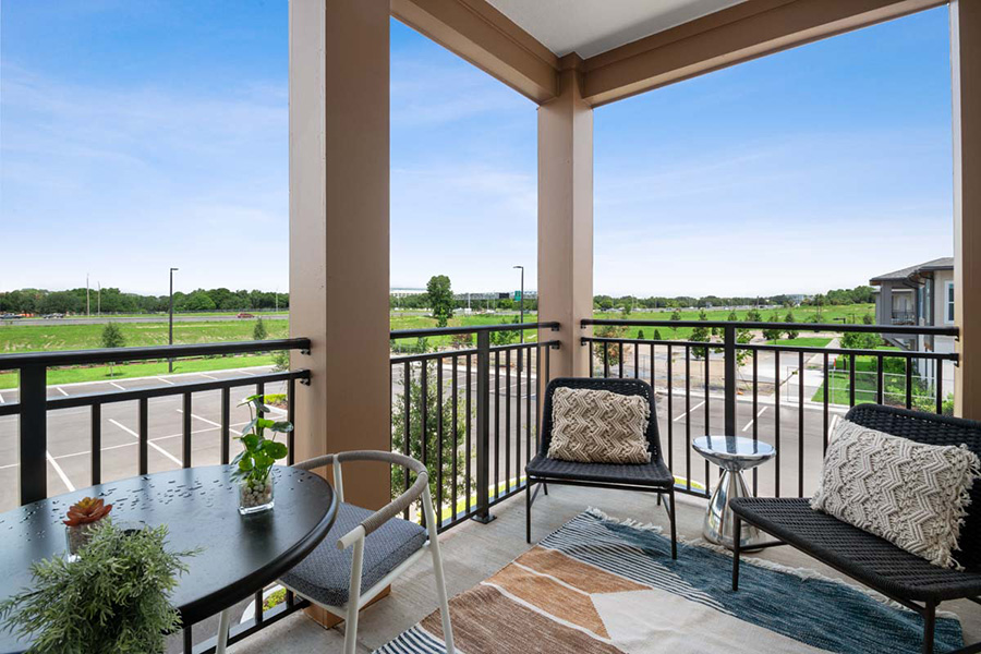Balcony with outdoor chairs, tables with plants, and rug.
