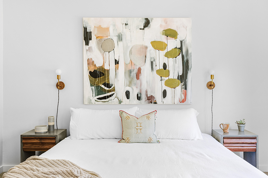 Bedroom with plush bed, bedside tables with decor, lamps, and abstract artwork.