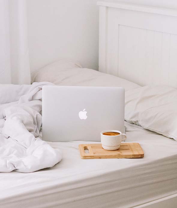 Plush white bed with laptop computer and coffee mug.